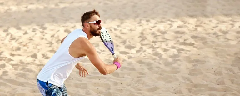 Immagine dinamica di un giovane che gioca a beach tennis, colpendo la palla con la racchetta. Allenamento all'aperto in una calda giornata estiva. Vista dall'alto. Concetto di sport, tempo libero, stile di vita attivo, hobby, gioco, estate, pubblicità.