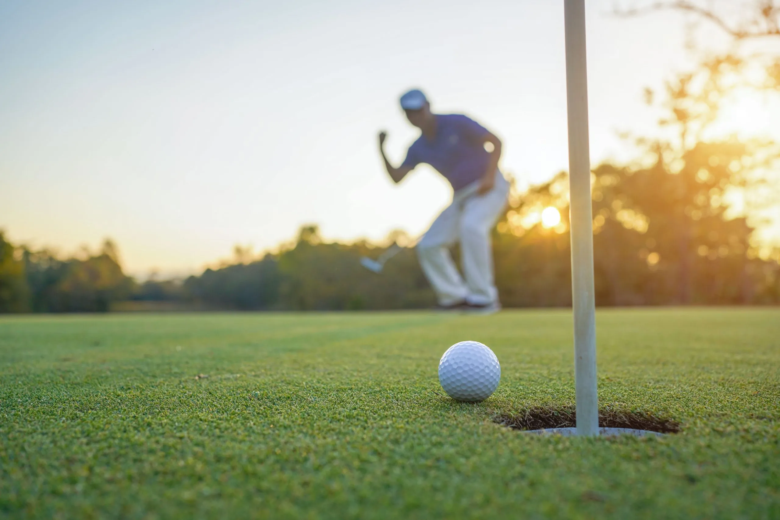 Azione del golfista per vincere dopo aver messo a lungo la palla da golf sul golf verde, lens flare sul sole impostato sera tempo.