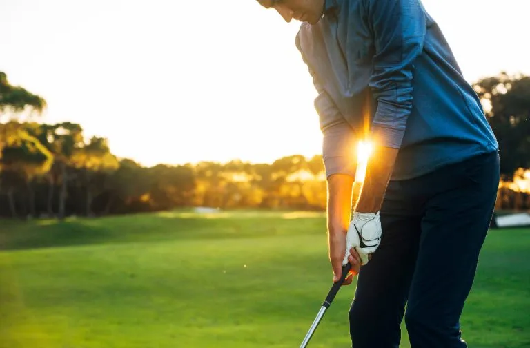 Männlicher Golfspieler beim Abschlagen des Golfballs vom Abschlagplatz bei schönem Sonnenuntergang