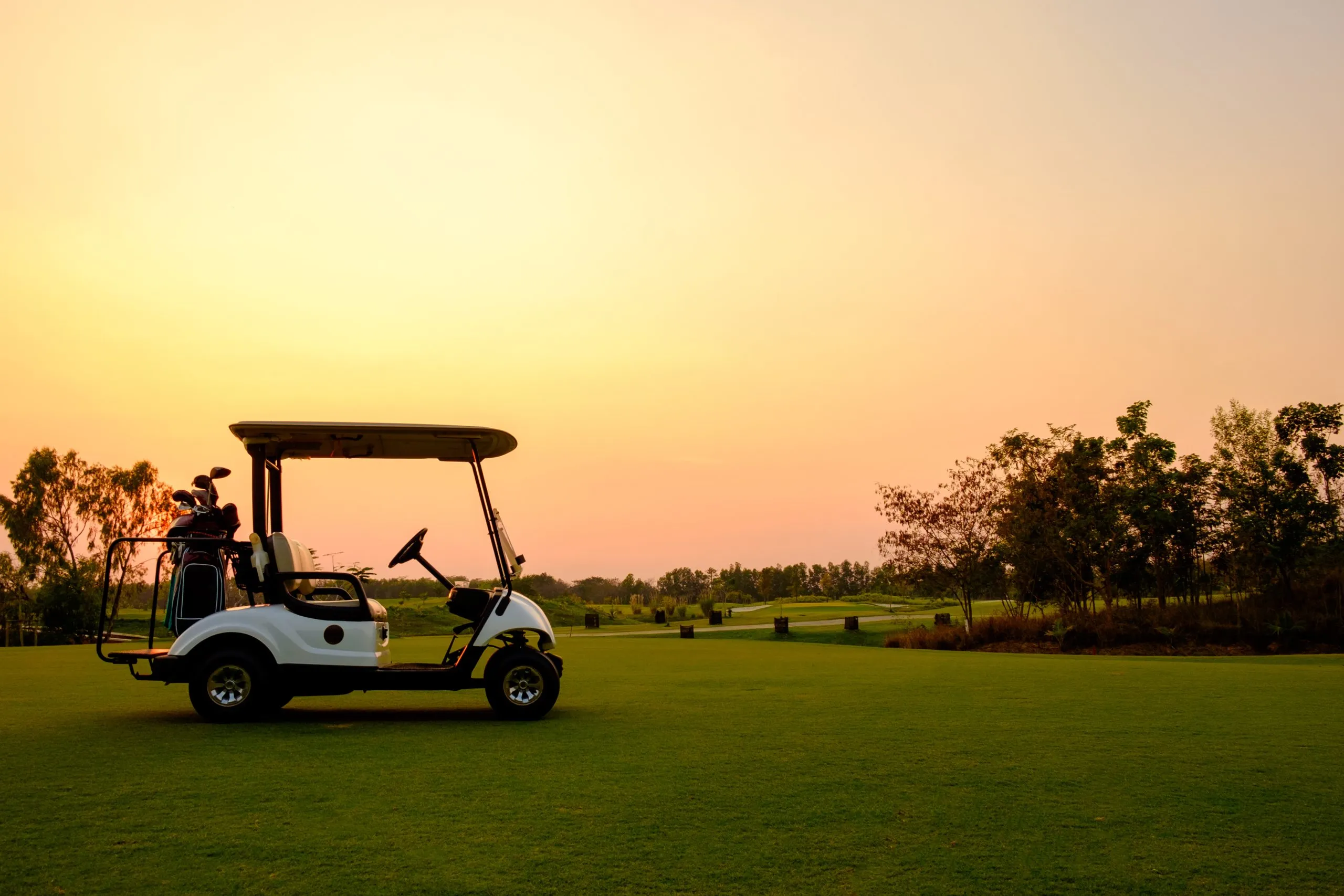 Golf Cart Auto in Fairway des Golfplatzes mit frischen grünen Gras Feld und Wolke Himmel und Baum auf Sonnenuntergang Zeit