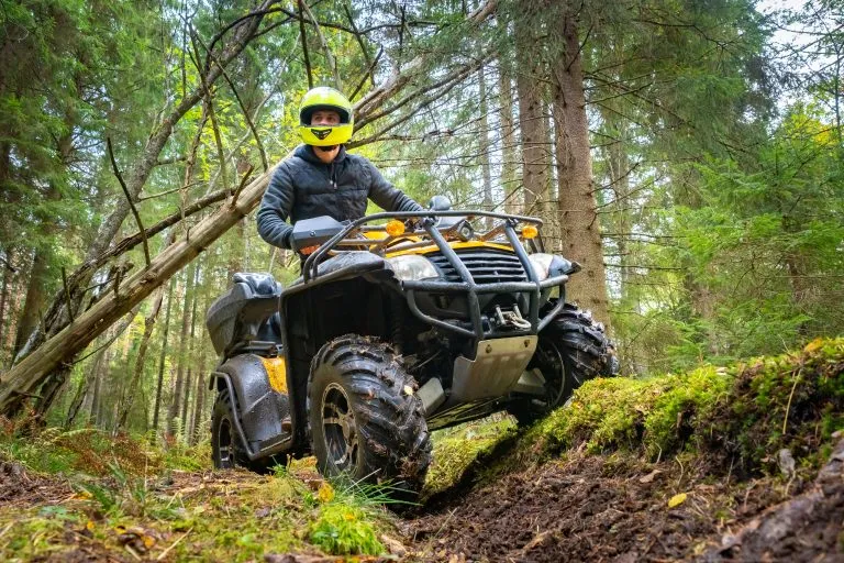 Ein Mann mit einem gelben Helm fährt auf einem Quad durch den Wald. Quad-Bike auf einem Waldweg. Fahrt durch den Wald mit einem Quad. Verkauf und Vermietung von ATVs. Fahren auf schlechten Straßen.